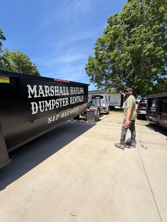 A crew member walking beside a lettered Marshall Hauling rental dumpster on a concrete pad