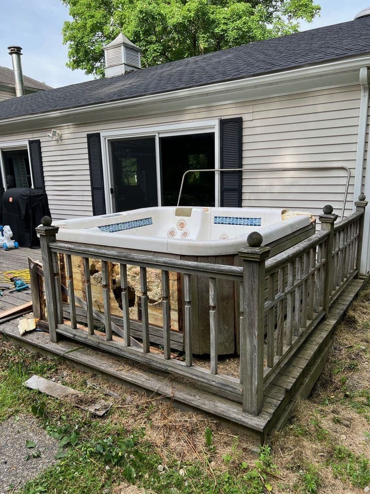 A weathered hot tub still sitting on a backyard deck before removal