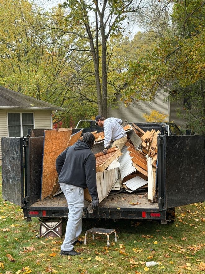 Two crew members loading torn-out lumber and doors into the dump trailer