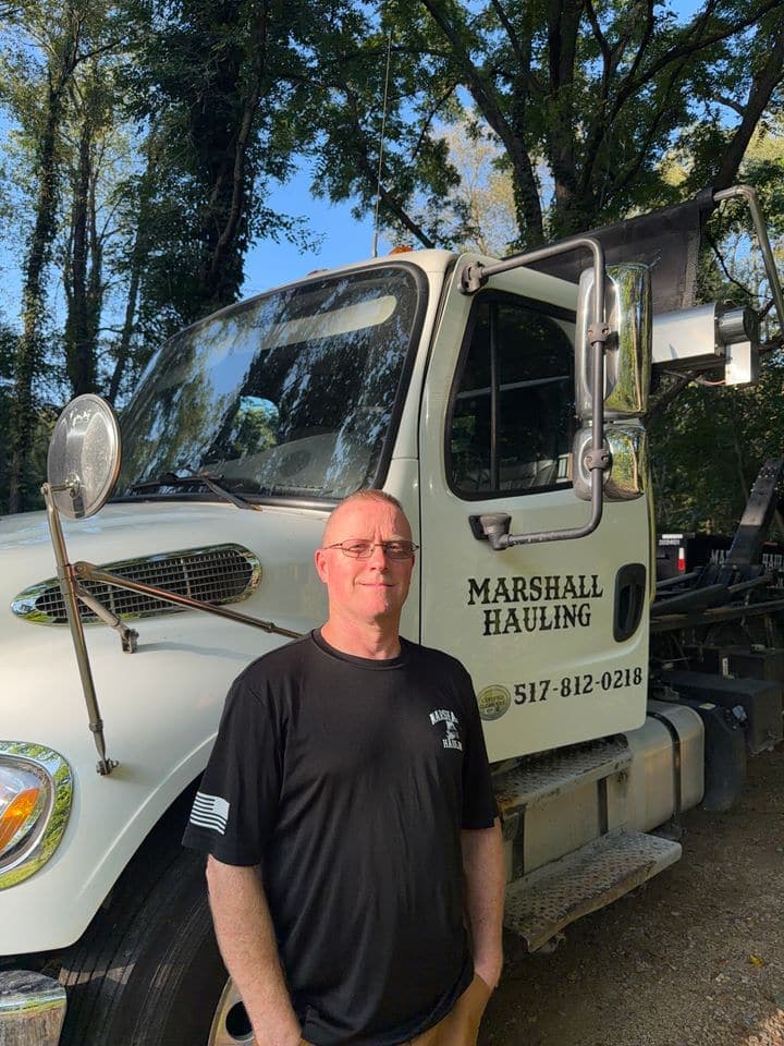 Todd in front of the white Marshall Hauling truck, with the company name and phone number on the door