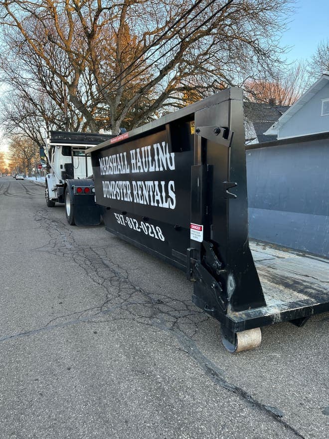 A Marshall Hauling roll-off dumpster being set down off the delivery truck on a residential street